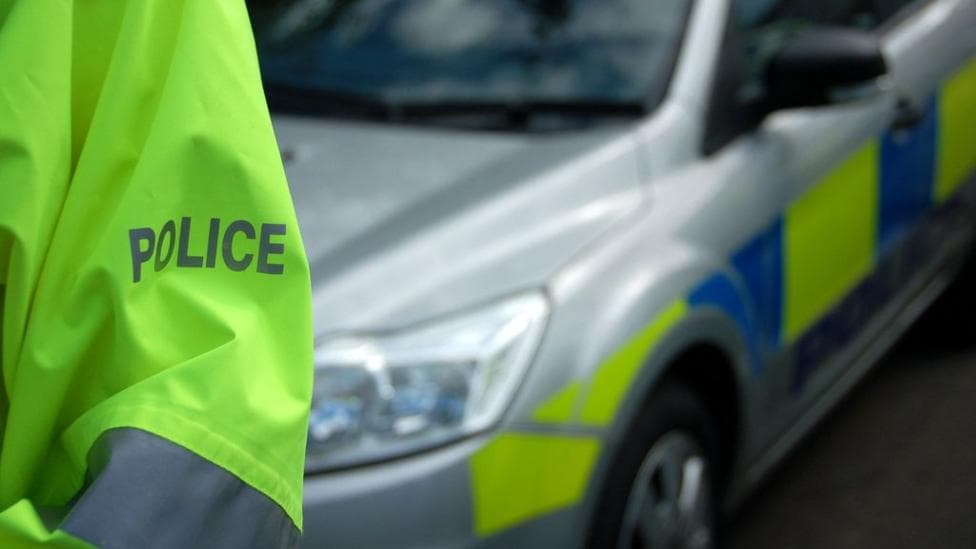 Police officer's arm in a hi-vis jacket with a police car behind