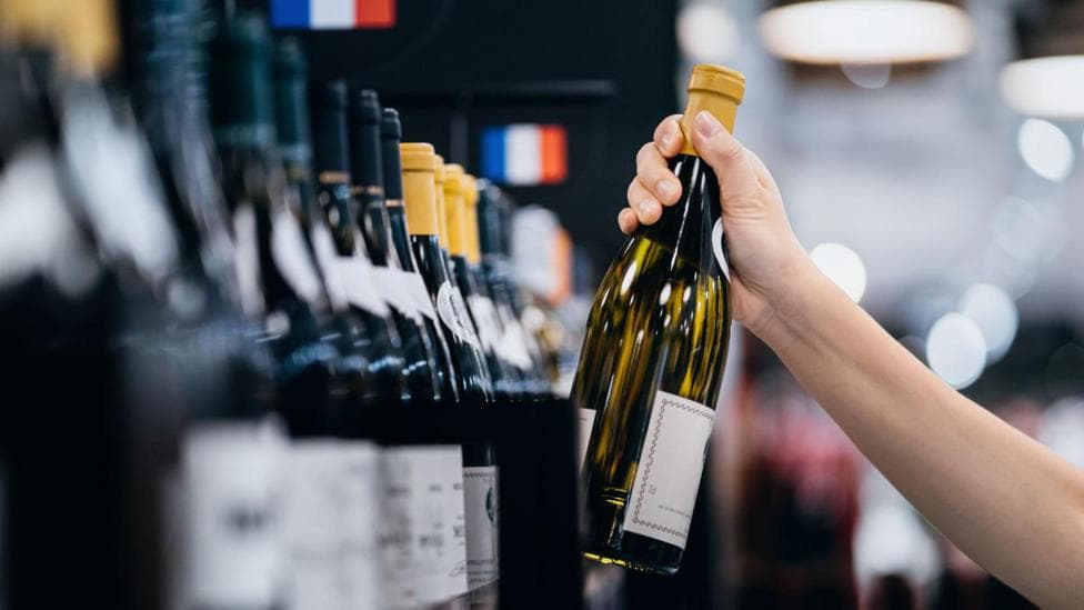 A person takes a glass bottle of wine off of a supermarket shelf