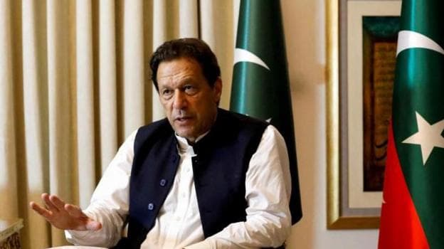 Former Pakistani Prime Minister Imran Khan speaks with Reuters during an interview, in Lahore, Pakistan March 17, 2023. He can be seen seated with his hand outstretched and speaking. Two Pakistani flags are behind him