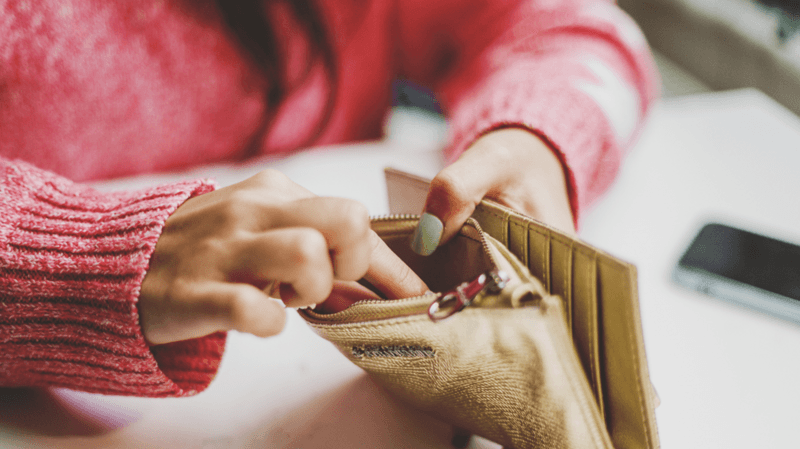 Person with red jumper has fingers inside gold coloured wallet.