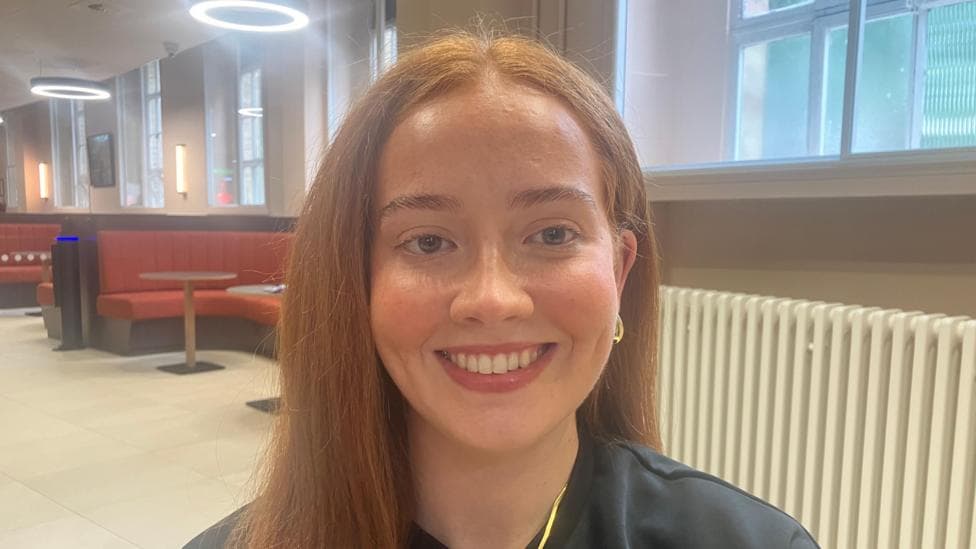 A young woman, Keri Teague. She is wearing a black top with a gold necklace and gold earrings.
She has long auburn hair.