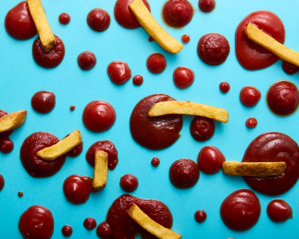 French fries and pools of ketchup in various sizes arranged on a blue surface