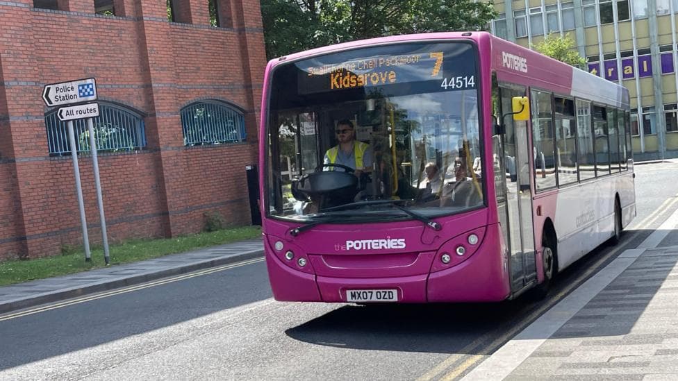 A purple and white bus with "7 Kidsgrove" on the screen at the top drives towards us along a road.