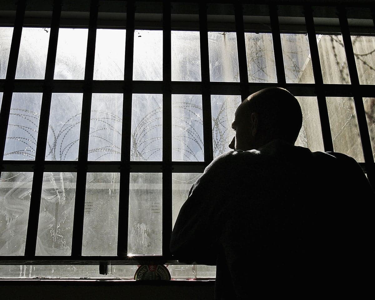 Silhouette of a male prisoner looking out of the window of his cell