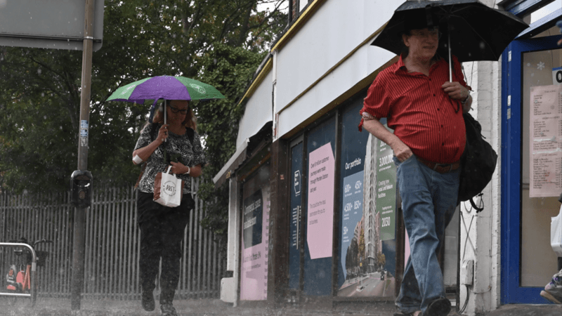 A man and a woman walk through torrential rain while holding umbrellas