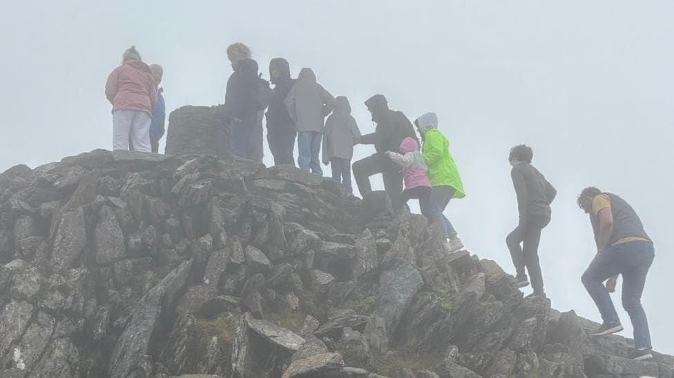A line of people waiting to reach the trig point at the peak of Yr Wyddfa on a misty day