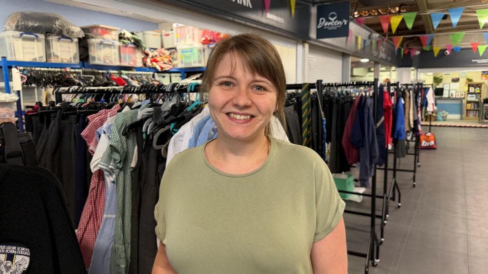 Ashleigh Hirst standing in the charity's uniform store, smiling at the camera. She has brown hair tied back and a fringe. She is wearing a green T-shirt.