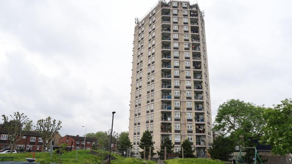 A tall beige tower block sits just behind a child's playground.