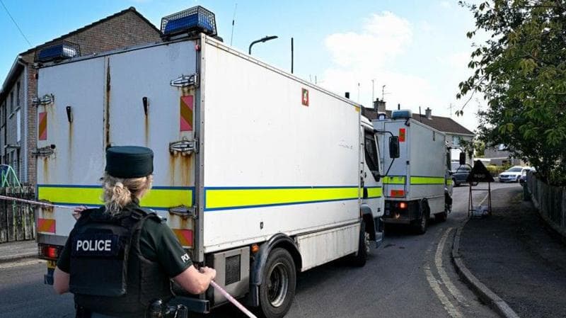 White and yellow security vehicles and a police officer in dark clothing with blonde hair at scene of alert in Gardenville Avenue, Omagh.