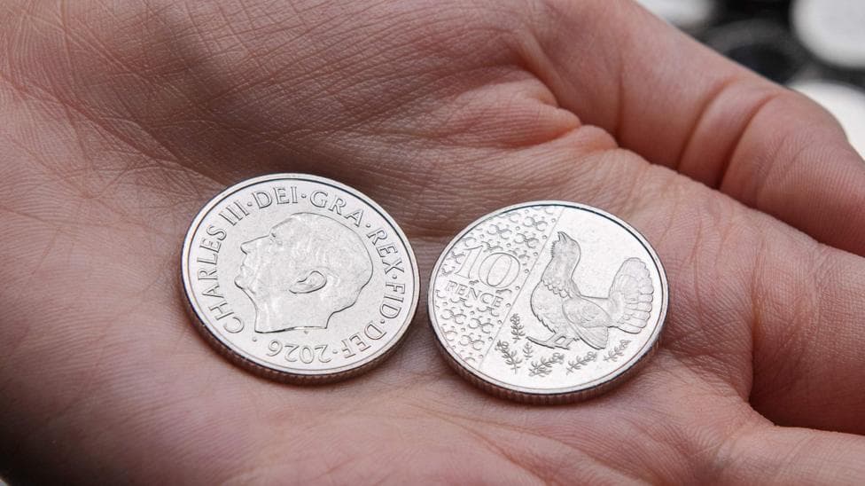 New 10p coin in the palm of someone's hand with one coin on the side showing an image of King Charles and dated 2026, with another coin on the reverse side showing a capercaillie.