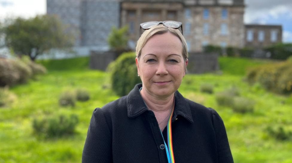 NHS Grampian chief executive Laura Skaife-Knight is standing outside. Dr Gray's hospital is in the background. Skaife-Knight has blonde hair tied up and glasses on her head. She is wearing a black coat and multi-coloured lanyard.