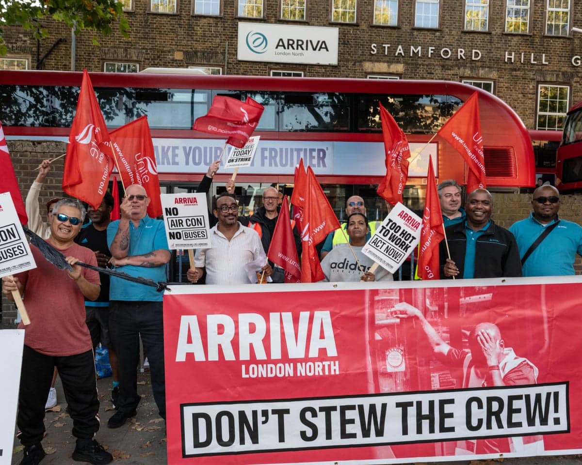 Striking Arriva bus drivers wave red union flags and hold protest signs at a picket line