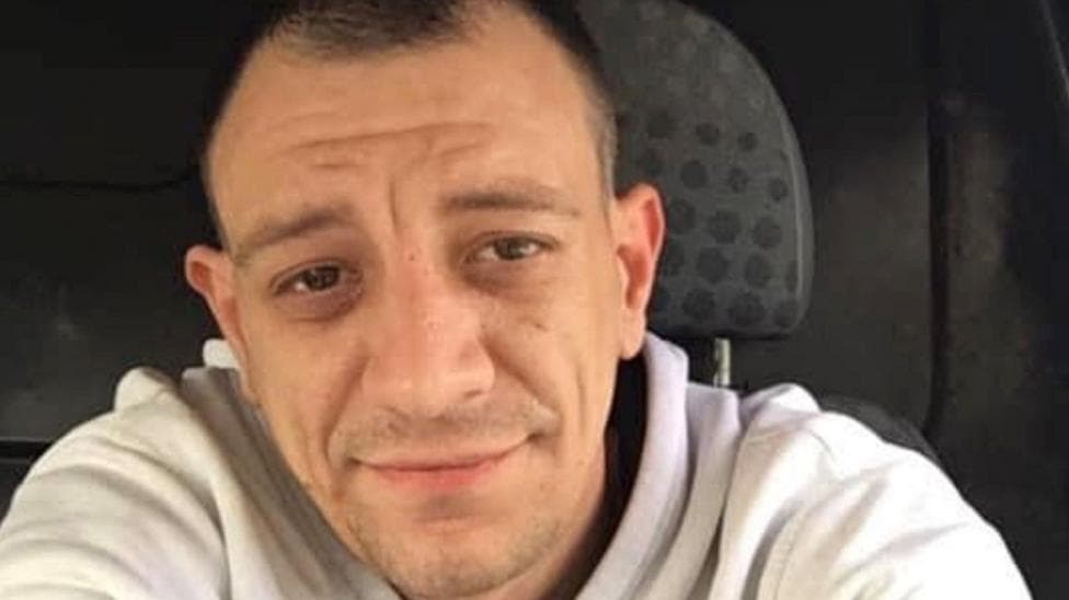 George Robertson looking straight at the camera. He is wearing a light grey hoodie. He is smiling and appeared to be sitting in a van.