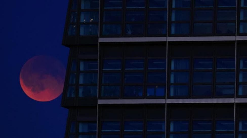 A red Moon lurking behind a glass skyscraper.