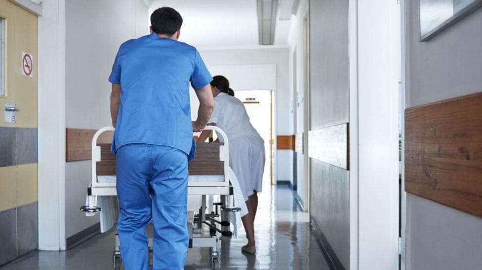 Rearview shot of hospital staff wheeling a patient in a gurney down a corridor