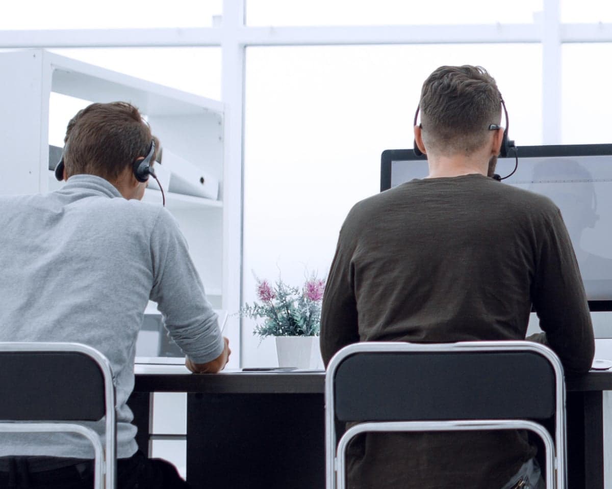 Two call centre workers wearing headsets at a desk with a screen on it