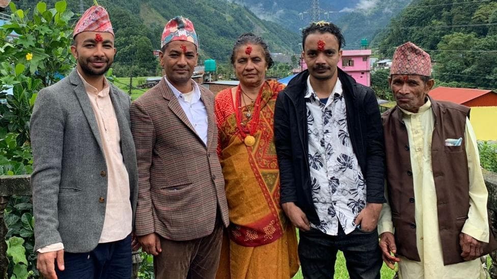 Four men and one woman side-by-side posing for a picture. There are green mountains behind them.