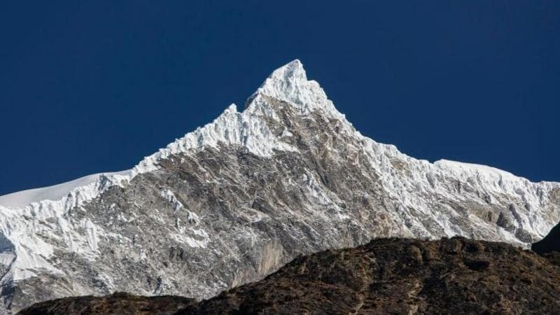 A panomanic view of the Langtang Lirung peak. The snowy summit is seen against a clear blue sky.