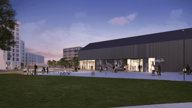 An artist's impression of the future Art Works development in Granton, showing a render of a building with a sloping roof, brown frontage and bright lights on inside and people walking near a patch of grass.