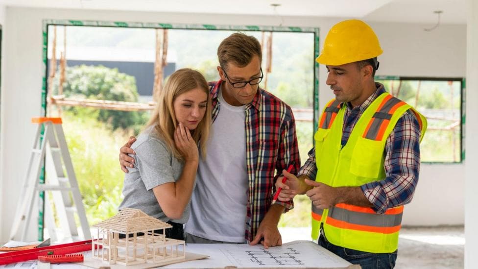 A couple looks at plans with a builder in their home, which is under renovation
