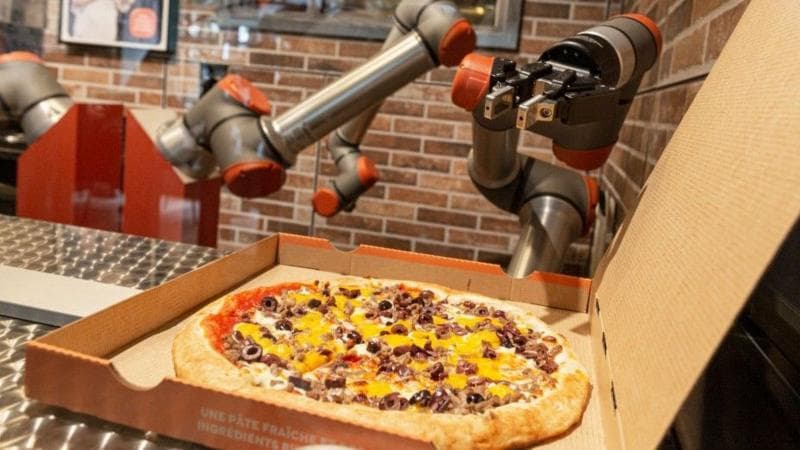 A robot arm hovers over a pizza