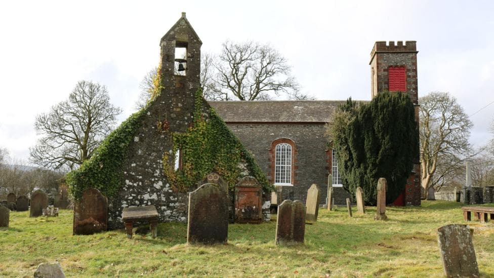 Two churches, one old and ruined in the foreground with a bell tower and the other a little more modern and well kept behind it. There are gravestones and trees around it