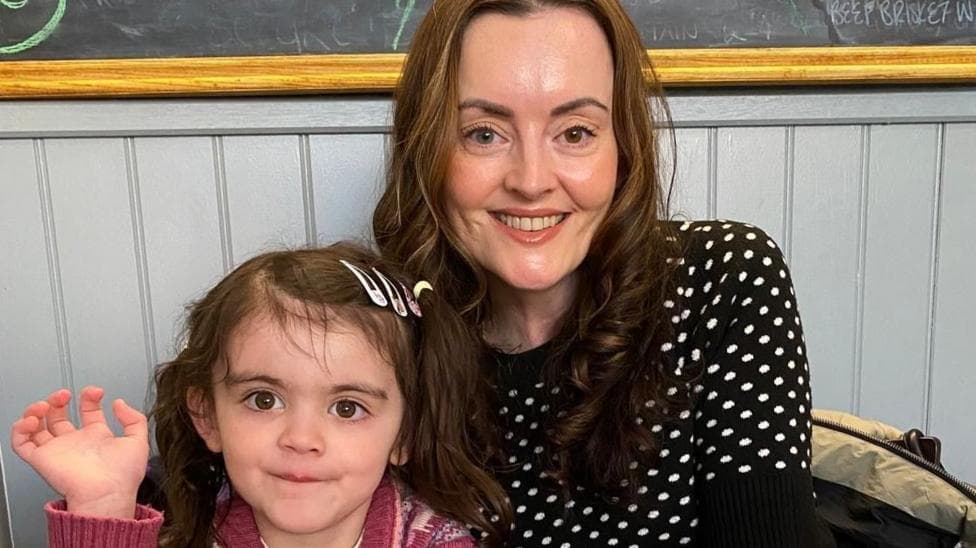 Maeve Mackinnon, wearing a black and white polka-dot top, and her daughter Màili, aged 4, in a pink cardigan with bunches, waving at the camera