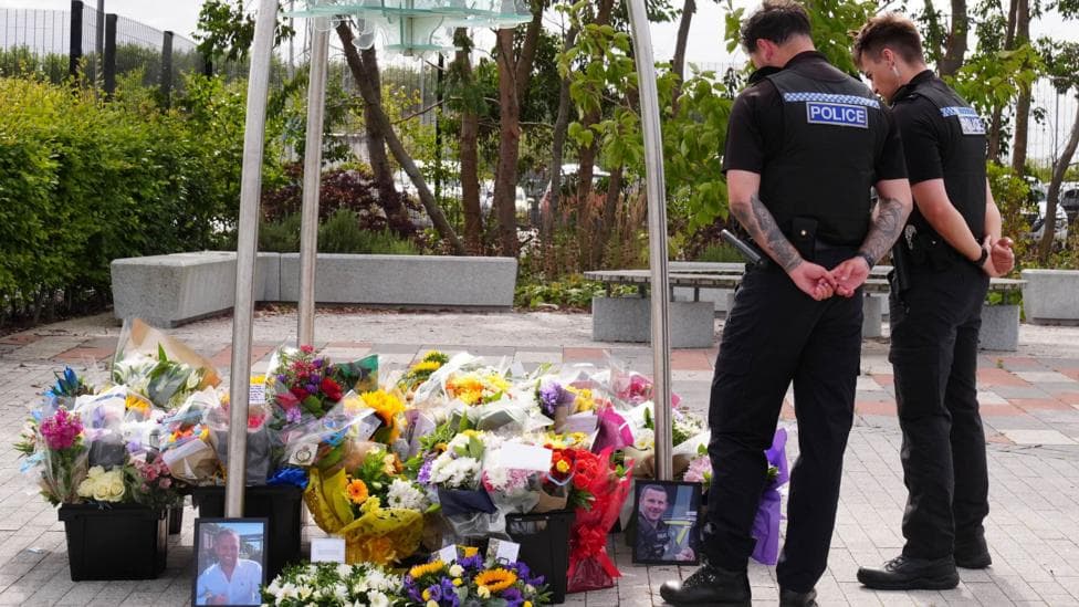 Police officers look at flowers at the Cleveland Police HQ in Middlesbrough. There are pictures of PC Matthew Blades and PC Tom Clough among the flowers.