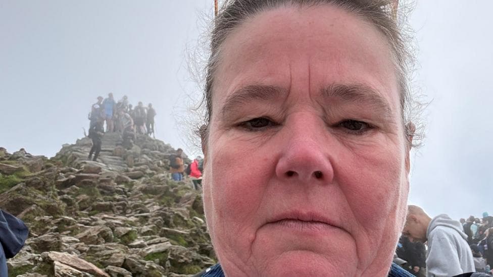Helen has a neutral expression as she takes a selfie overlooking the summit of Yr Wyddfa