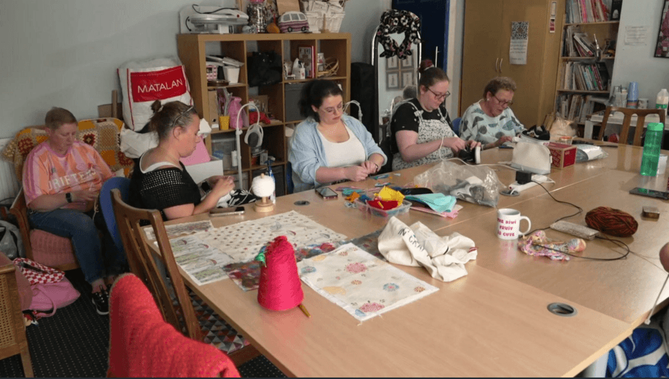 A group of women sat around a table knitting and sewing.