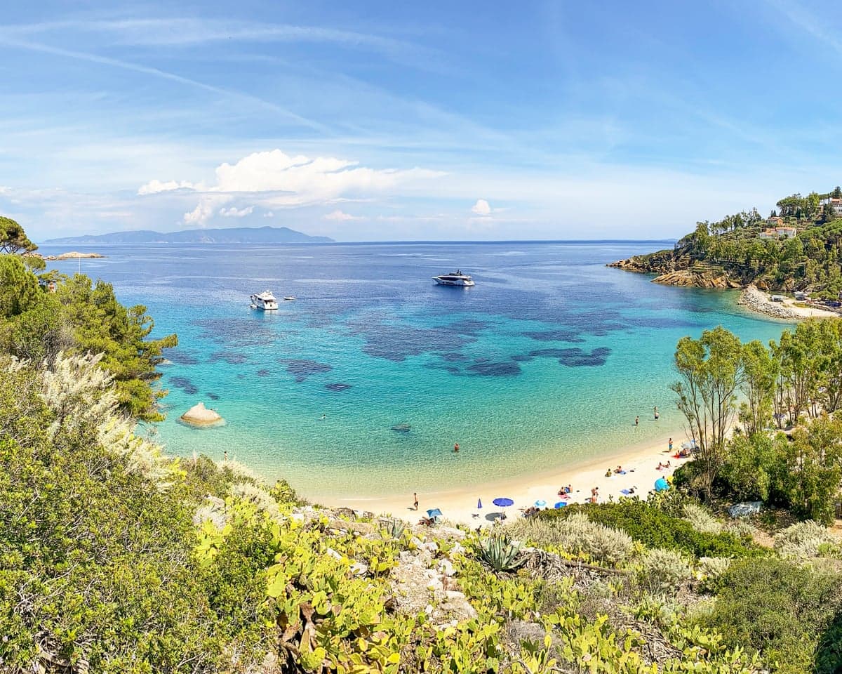 Cannelle beach curves along a turquoise bay on Isola del Giglio, with boats anchored offshore