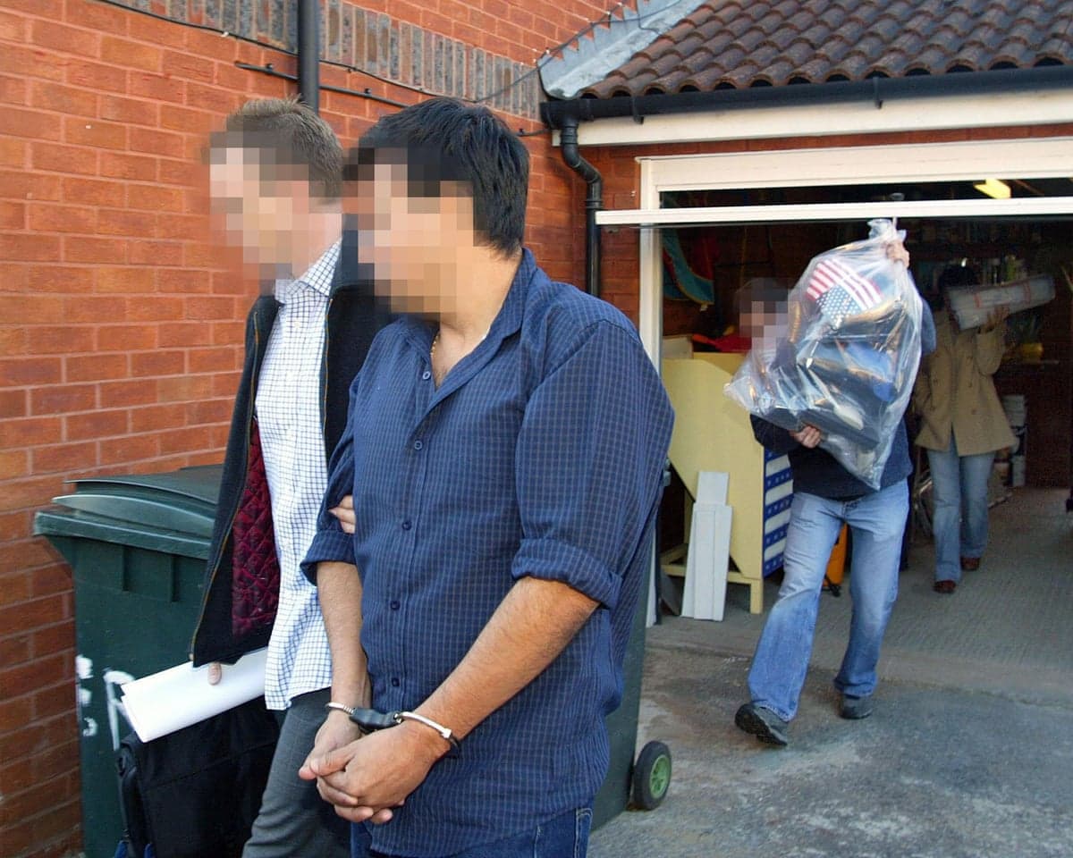 Police officers escort an arrested man and carry away evidence after a dawn raid on a property in east London.