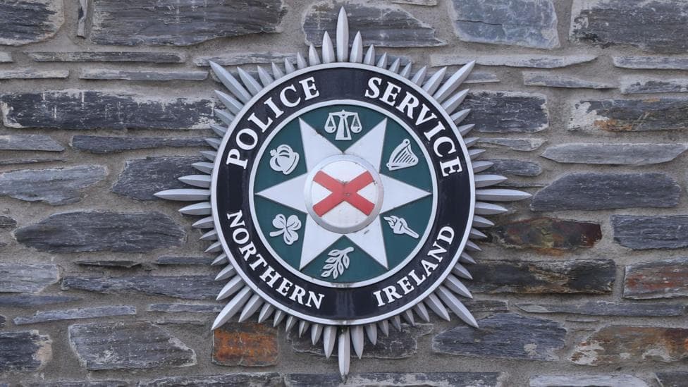 A black, green and grey PSNI crest on a wall.