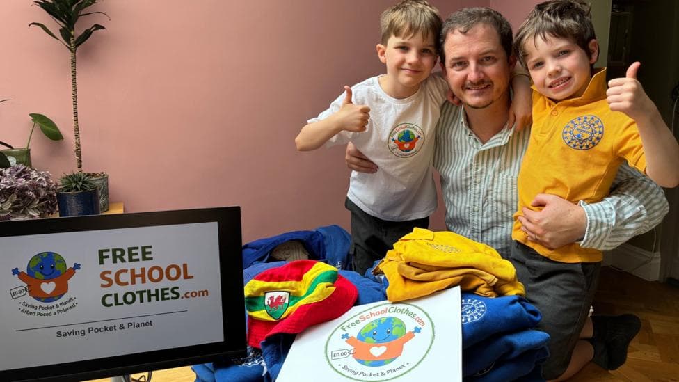 Jon who is 42 is pictured with his two children 10 year old Tom and six year old, Sion in amongst several blue school jumpers and several yellow polo shirts from Ysgol Treganna primary school next to a computer open on the Free school clothes website .