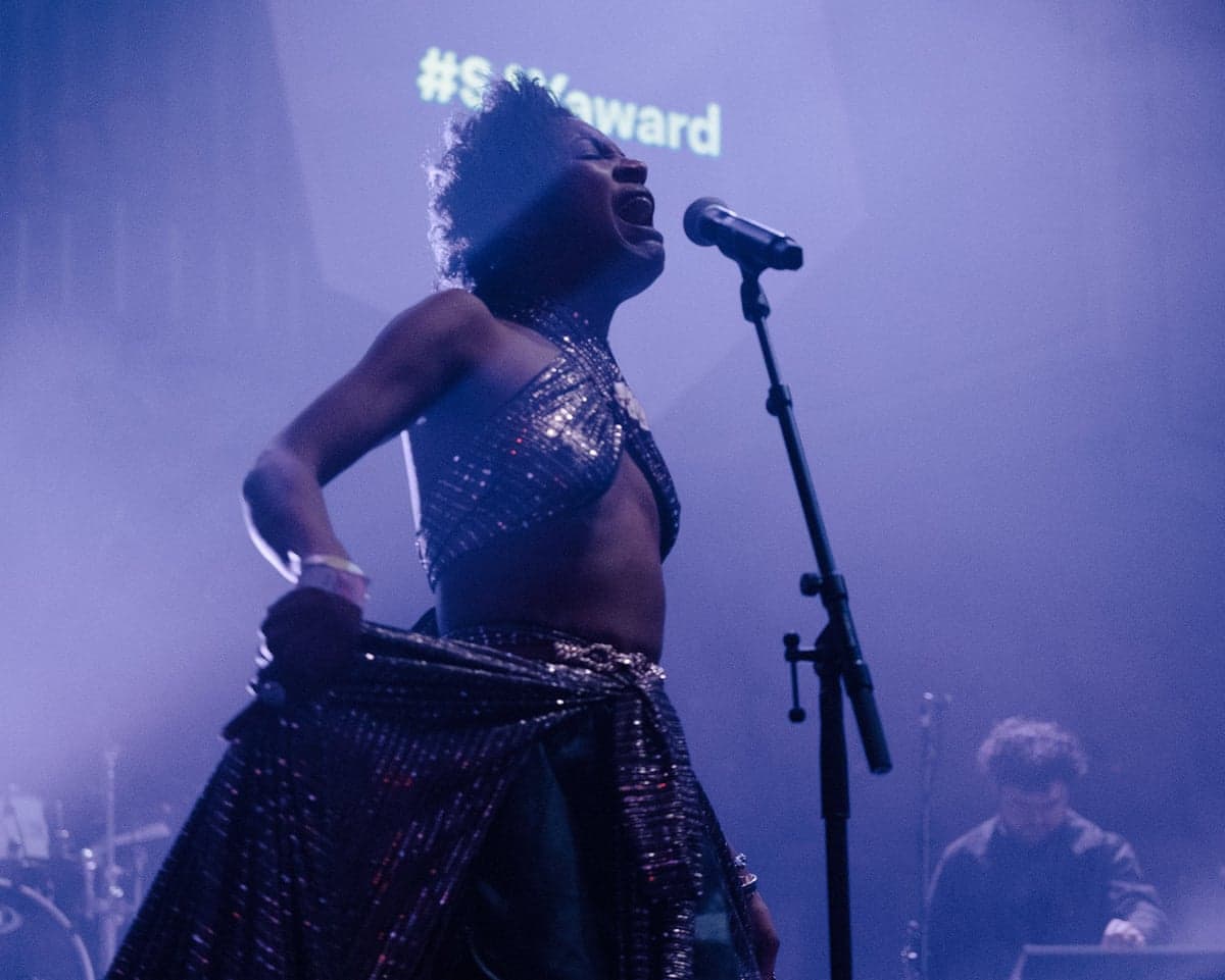 Beldina Odenyo in a sequined outfit sings passionately into a microphone on stage