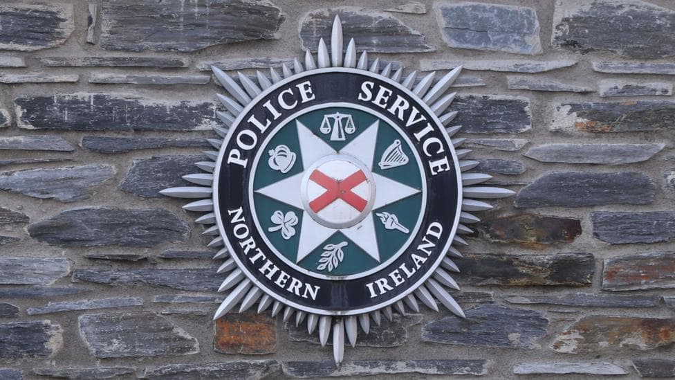 A PSNI logo on a grey brick wall.