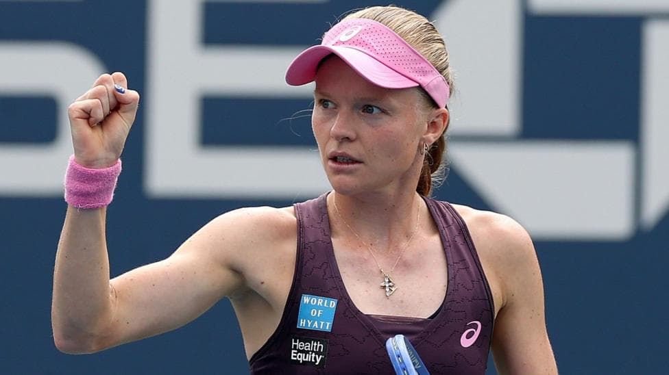 Harriet Dart, wearing a purple dress and pink visor, holds her racquet in her left hand and raises a clenched right fist