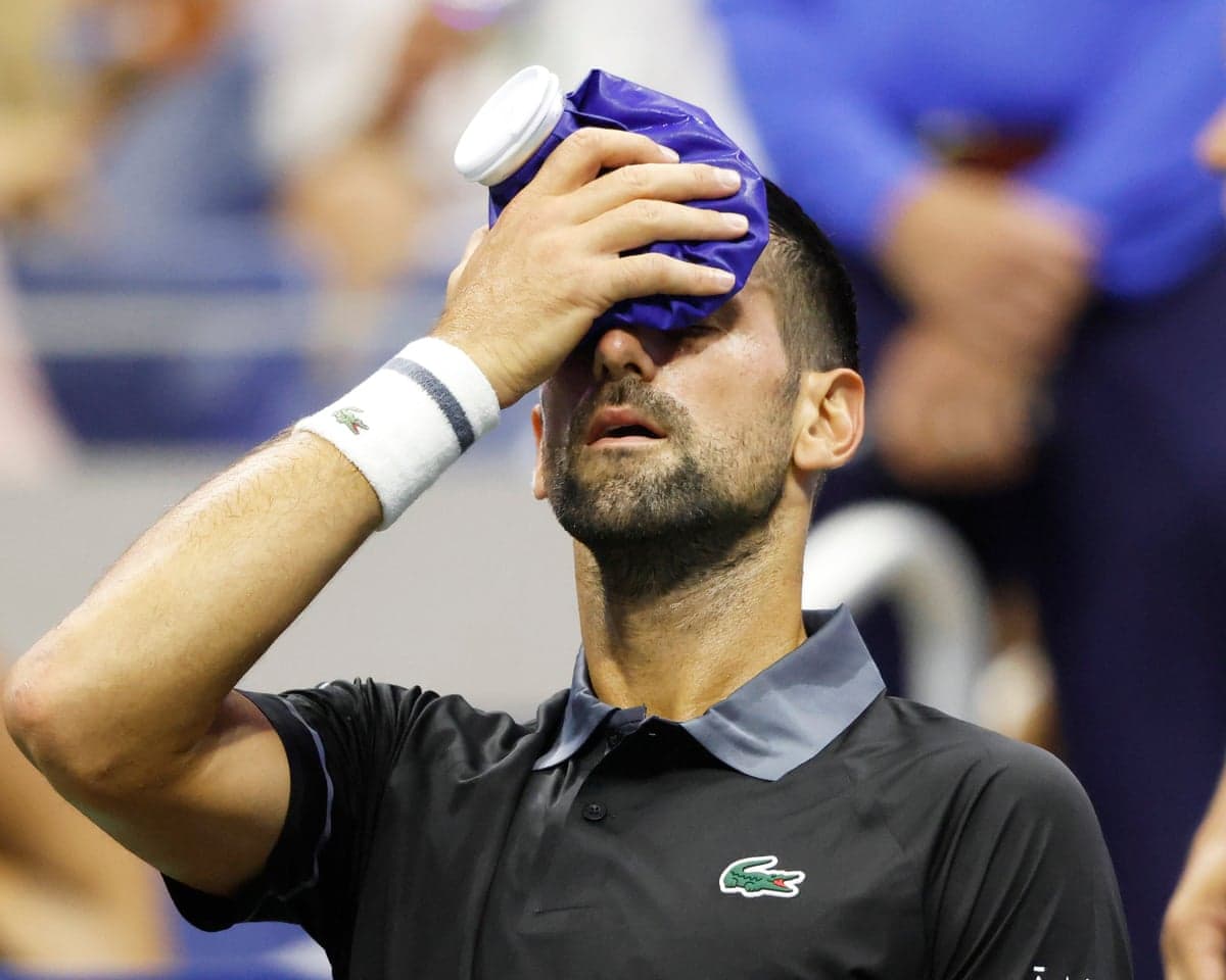 Novak Djokovic holds an ice pack to his forehead while seated at a change of ends
