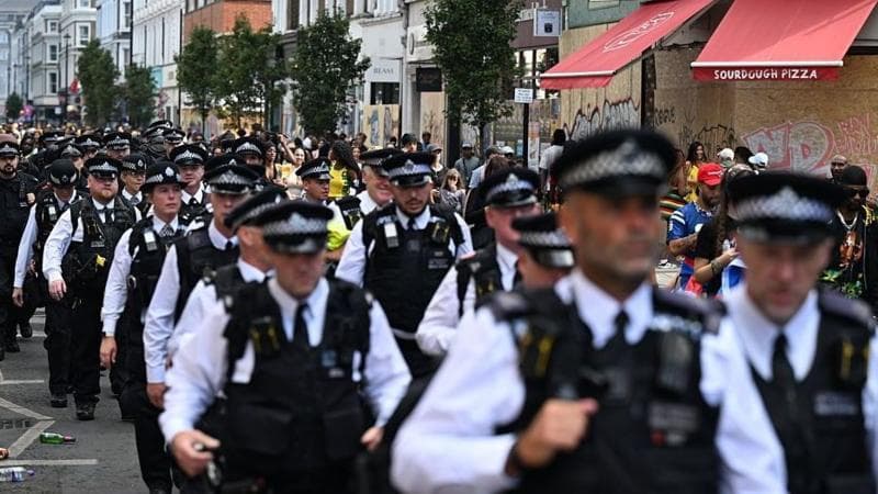 Dozens of members of the Metropolitan Police walk in uniform through the Notting Hill Carnival