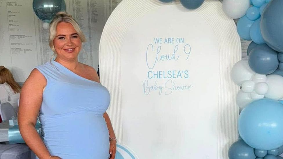 Chelsea McGillivray. She is wearing a blue one-shoulder dress and her blonde hair is tied into a bun. She is smiling at the camera.