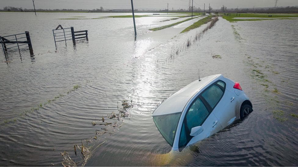 Car partially submerged, surrounded by flooded fields following Storm Chandra