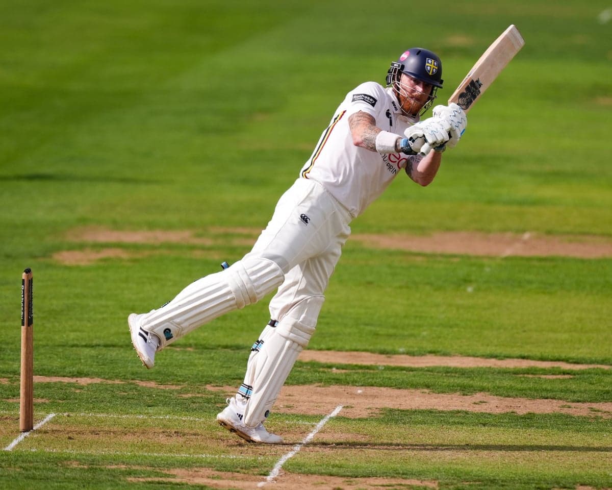 Ben Stokes, batting for Durham, swings his bat mid-stroke on the pitch.
