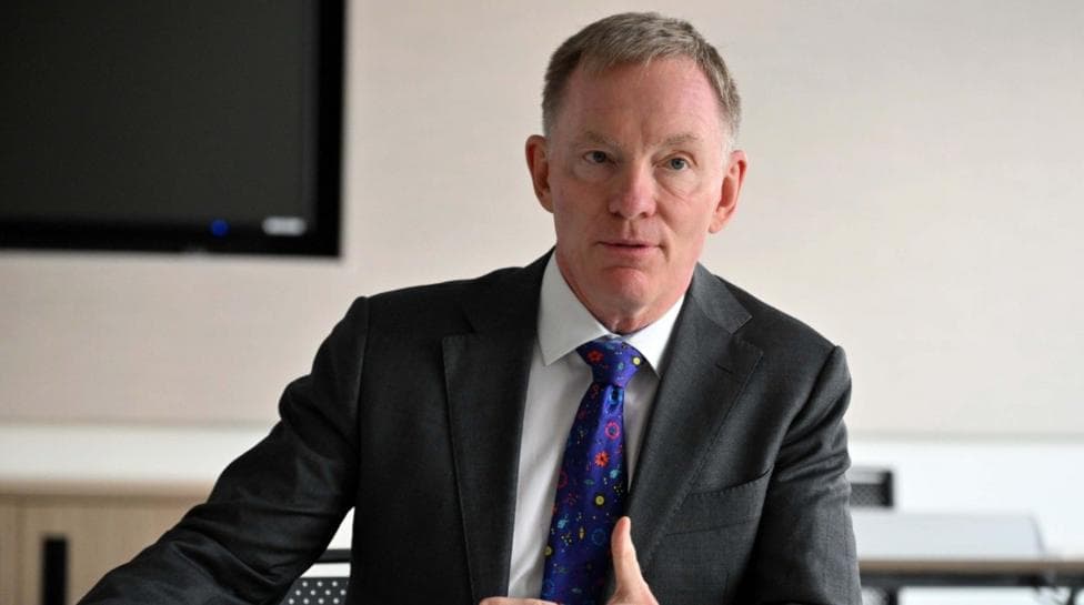 Sir Chris Bryant, with short dark grey hair, wearing a white shirt, blue tie and dark grey suit.