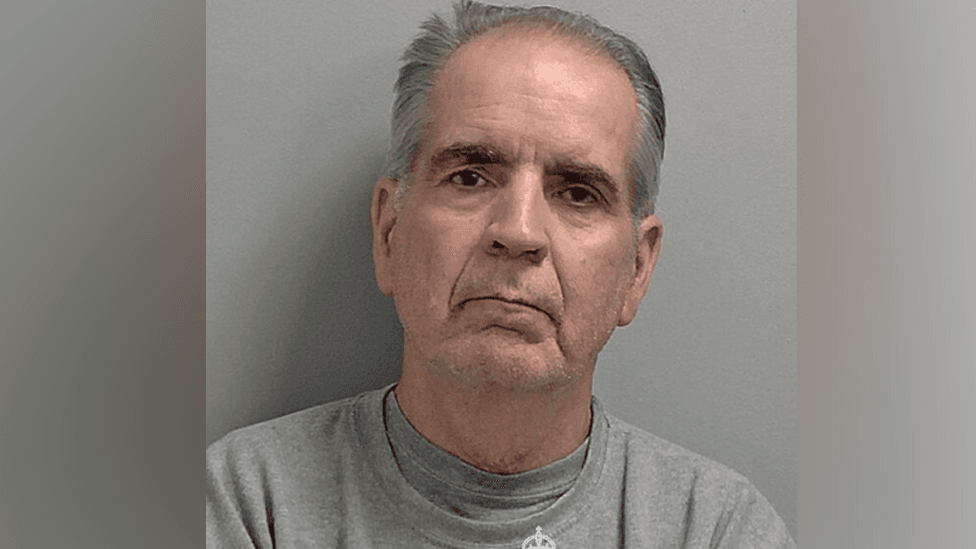 A police mugshot of Robert Alexander in a grey prison sweatshirt.