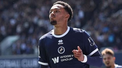Femi Azeez, wearing Millwall's dark blue home kit, points to some fans during a goal celebration
