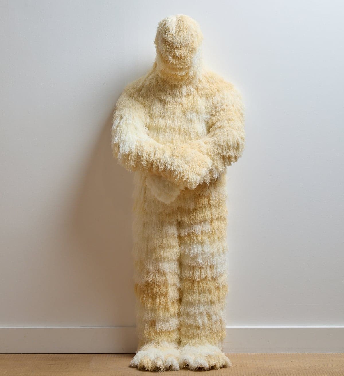 Sculpture by Woo Jin Joo of a figure covered in shaggy cream fibers, arms crossed