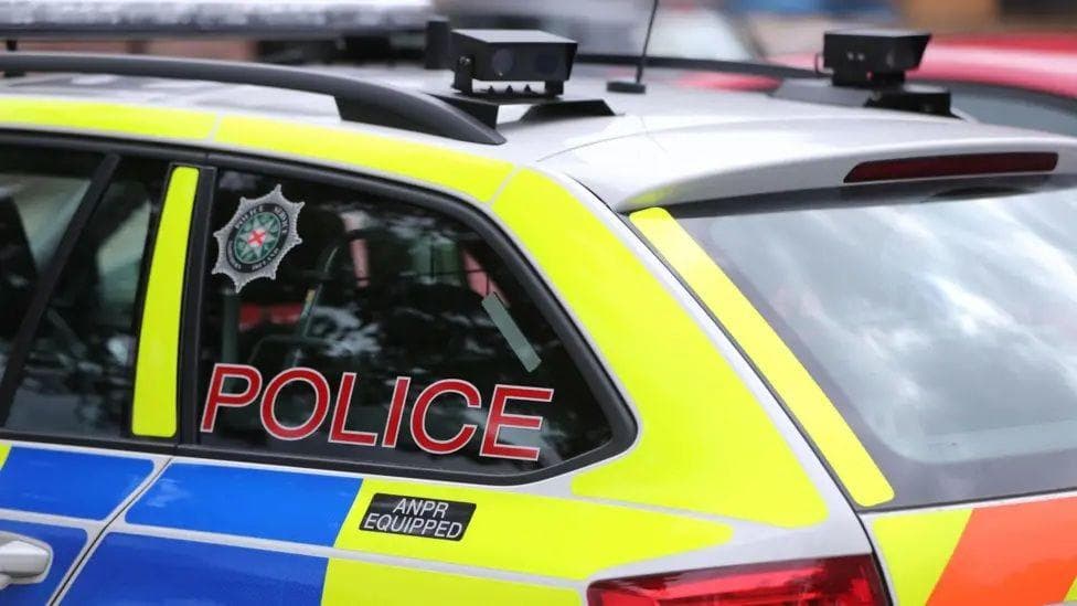 The rear of a PSNI car, yellow, blue and silver. Across the window says: 'POLICE'.