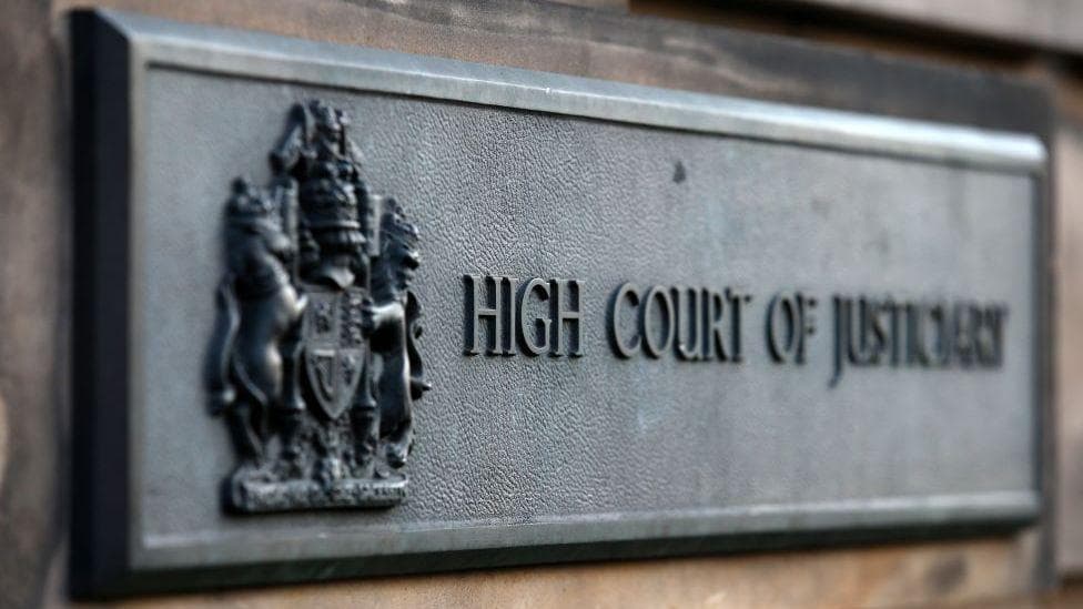 A grey sign on a building, which reads High Court of Justiciary, in bold letters.