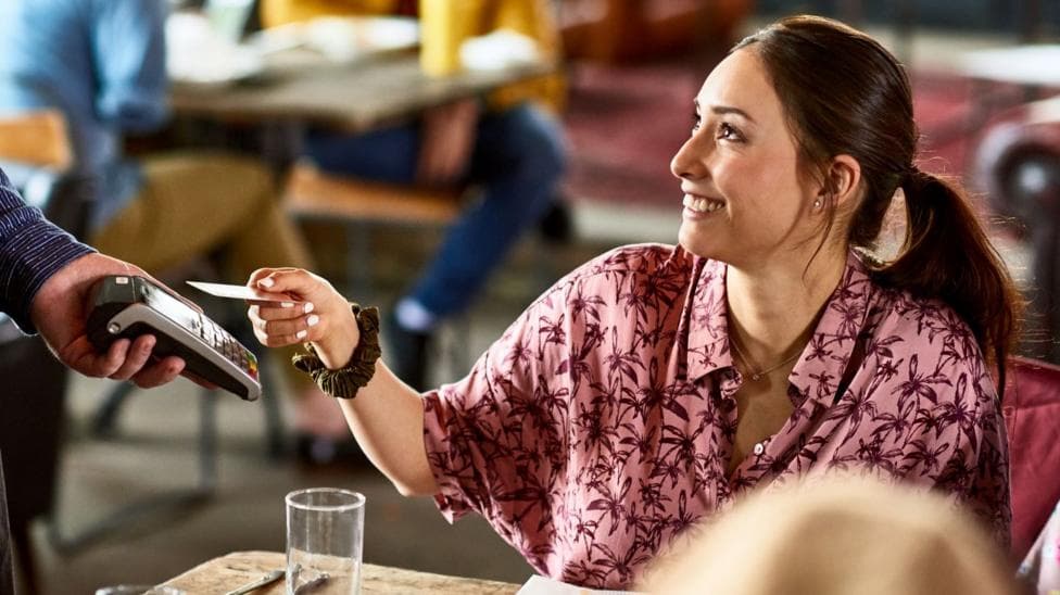 A woman in a pink shirt is paying for her meal with card.
