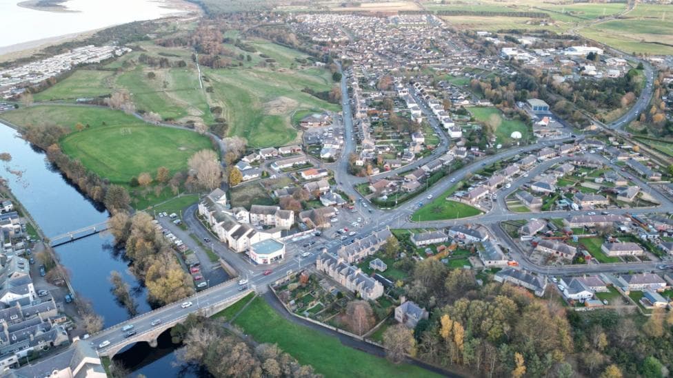 An aerial view of Nairn showing a road bridge carrying the A96 over the River Nairn, also rows of houses and part of the East Beach and the Inner Moray Firth.